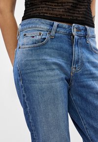 Jeansi din denim albastru cu croi drept, cusături din cupru și un etichetă mică de marcă pe buzunarul din spate. Material texturat cu un finisaj decolorat.