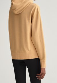Sweat à capuche de couleur beige clair, en tissu doux. Caractérisé par des poignets et un ourlet côtelés, une coupe décontractée et des détails de surpiqûres aux coutures.