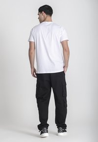 Bílý bavlněný tričko spárované s černými cargo kalhotami s několika bočními kapsami. Outfit doplňují černé tenisky s vzorovaným designem.