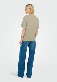T-shirt i bomuldsblanding i lys beige, med afslappet pasform og korte ærmer, parret med blå viddejeans med subtile syninger.
