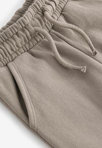 Hellgraue Sweatpants mit elastischem Bund und Kordelzug, weicher Textur, ausgestattet mit seitlichen Taschen und gesteppten Nahtakzenten.