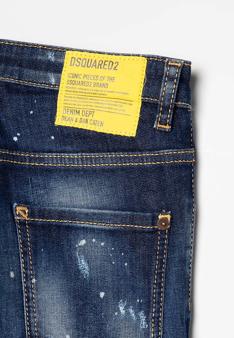 Jeans in denim blu scuro con un finish usurato, etichetta del marchio gialla, cuciture visibili e due tasche posteriori con dettagli in metallo.