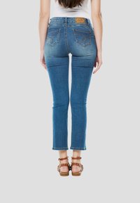 Blauwe denim jeans met een slanke pasvorm, iets ingekorte lengte en subtiele stikseldetails op de achterzakken. Voorzien van een bruine leren merkpatch.