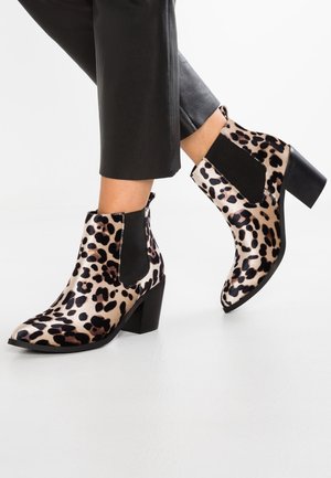 Bottines à imprimé léopard avec un talon carré, des panneaux latéraux en élastique noir et une texture lisse, sur fond clair.