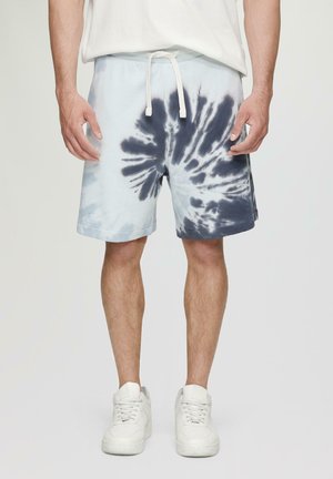 Hellblaue Tie-Dye-Shorts mit marineblauen Wirbelmustern, elastischem Bund, weißen Kordeln und umgeschlagenen Säumen, kombiniert mit weißen Sneakers.