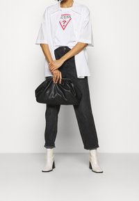 Sort lædertaske, hvid skjorte, grafisk t-shirt med rødt logo, mørke denim jeans og cremede ankelstøvler med blokhæle.