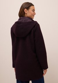 Manteau en polaire de couleur violet profond avec une capuche, surface texturée, manches longues et coupe droite. Présente des poches latérales et une doublure douce.