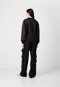 Sweatshirt preto com decote redondo e punhos elásticos, combinado com calças largas de cargo pretas com bolsos laterais e fechos de correr.