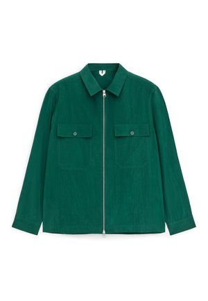 Veste longue à manches longues vert foncé avec col pointu, fermeture éclair intégrale à l'avant et deux poches poitrine à rabat avec bouton.