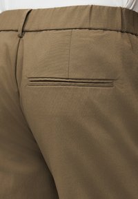 Κοντινό πλάνο χακί παντελονιού που δείχνει πίσω τσέπη με διακόσμηση welt, θηλιές για ζώνη και υφασμάτινη υφή.