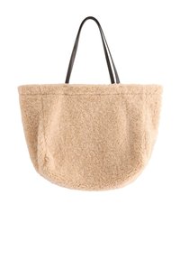 Beige, fluffig tote-väska med en plyschliknande textur; har långa svarta remmar; rund form med sidofickor för förvaring.