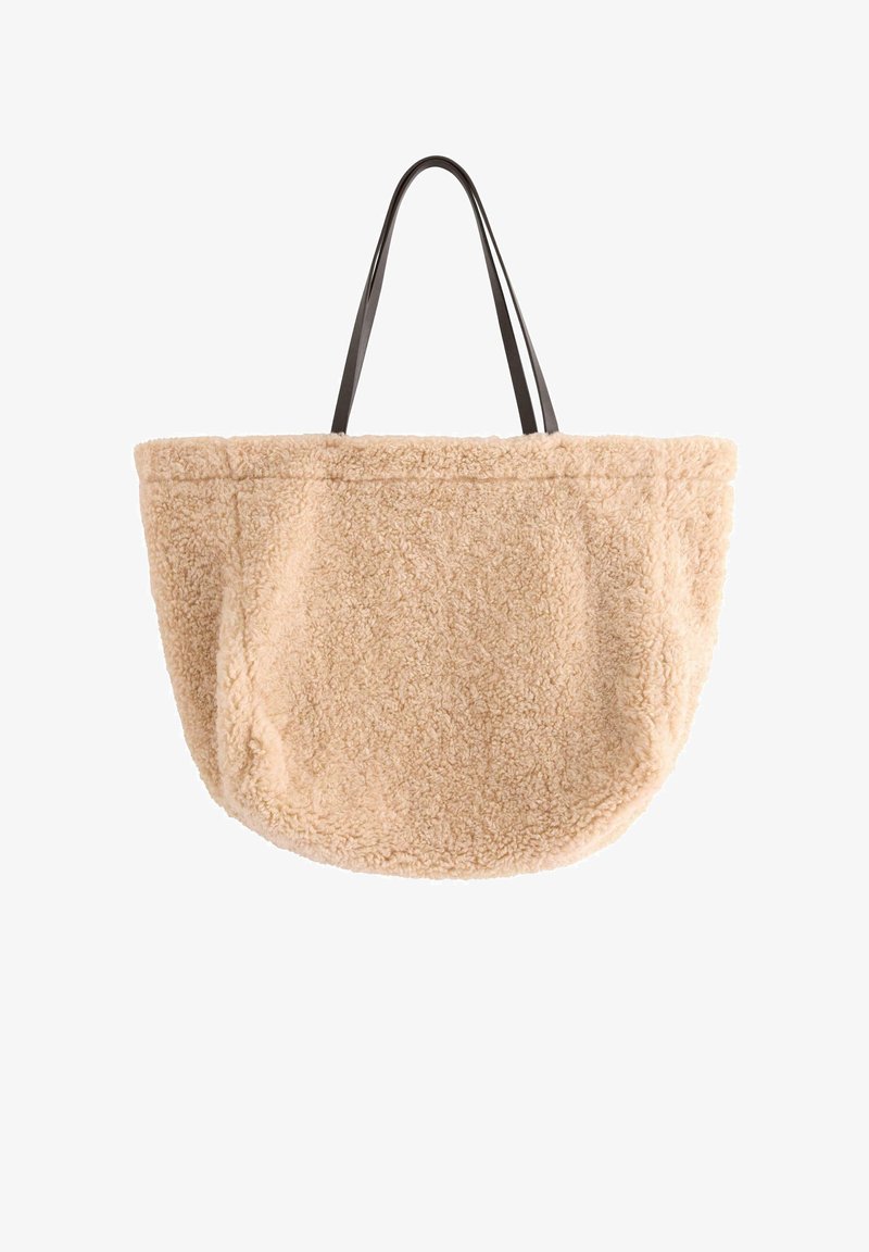 Beige, fluffig tote-väska med en plyschliknande textur; har långa svarta remmar; rund form med sidofickor för förvaring.