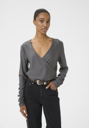 Gray wrap-style top with a deep V-neck and long sleeves, paired with black jeans and a textured brown belt featuring a silver buckle.