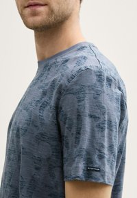Blue short-sleeve t-shirt featuring a subtle textured pattern. Made of soft fabric with a crew neckline and logo detail on the sleeve.