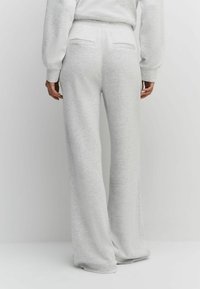 Light grey, high-waisted, wide-leg pants in soft, textured fabric with two back pockets. Finished hem with a relaxed, flowing fit.