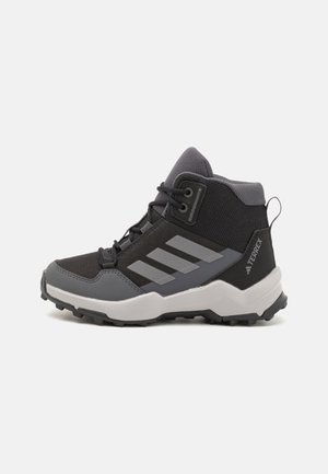 Sapatos de caminhadas em preto e cinza, com parte superior em tecido texturizado, sola de borracha e três franjas cinzas proeminentes de cada lado. Design de altura média.