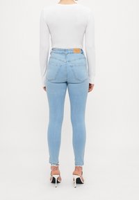 Ljusblå högmidjade jeans med en åtsittande silhuett, två bakfickor och en brun märkeslapp vid midjan. Matchat med en vit långärmad topp.