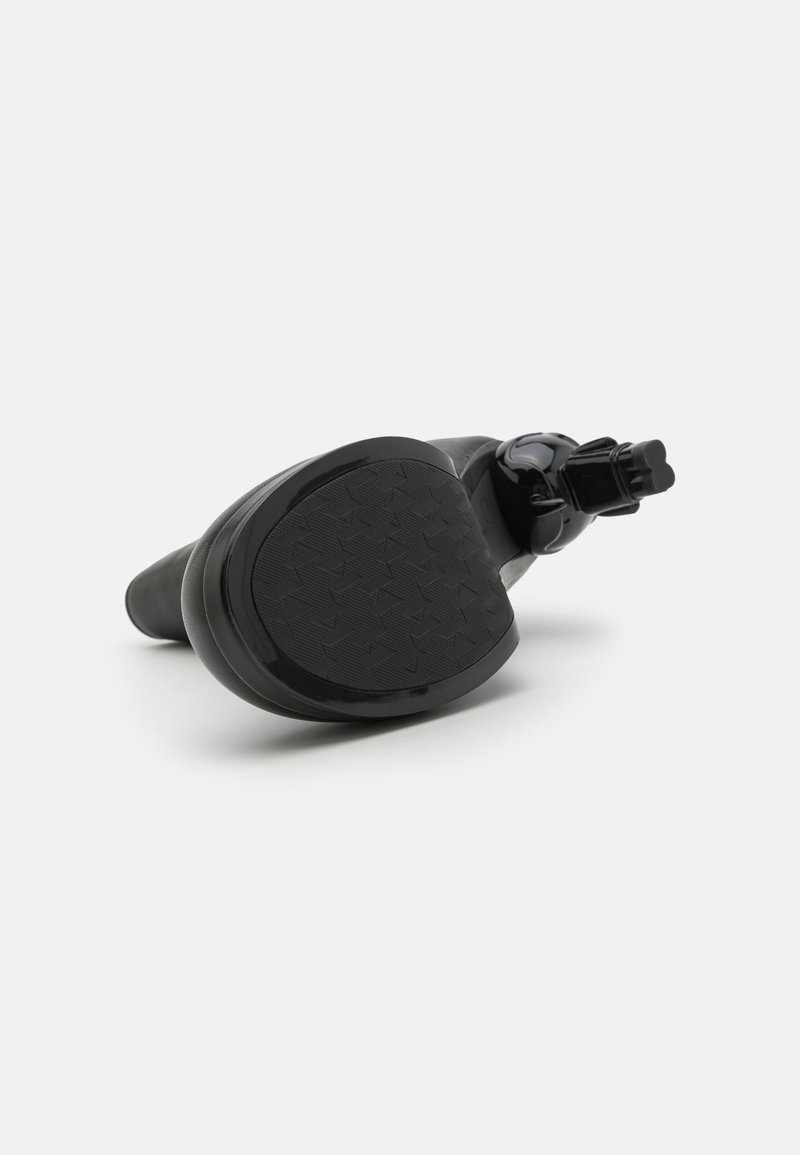 Semelle de chaussure en caoutchouc noir avec un motif texturé, dotée d'une sangle ajustable sécurisée et d'une forme lisse et courbée pour un meilleur ajustement.