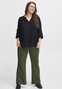 Svart, knappradig blus med trekvartslånga ärmar, ihopparad med olivgröna, vida byxor. Svarta skor fulländar outfiten.