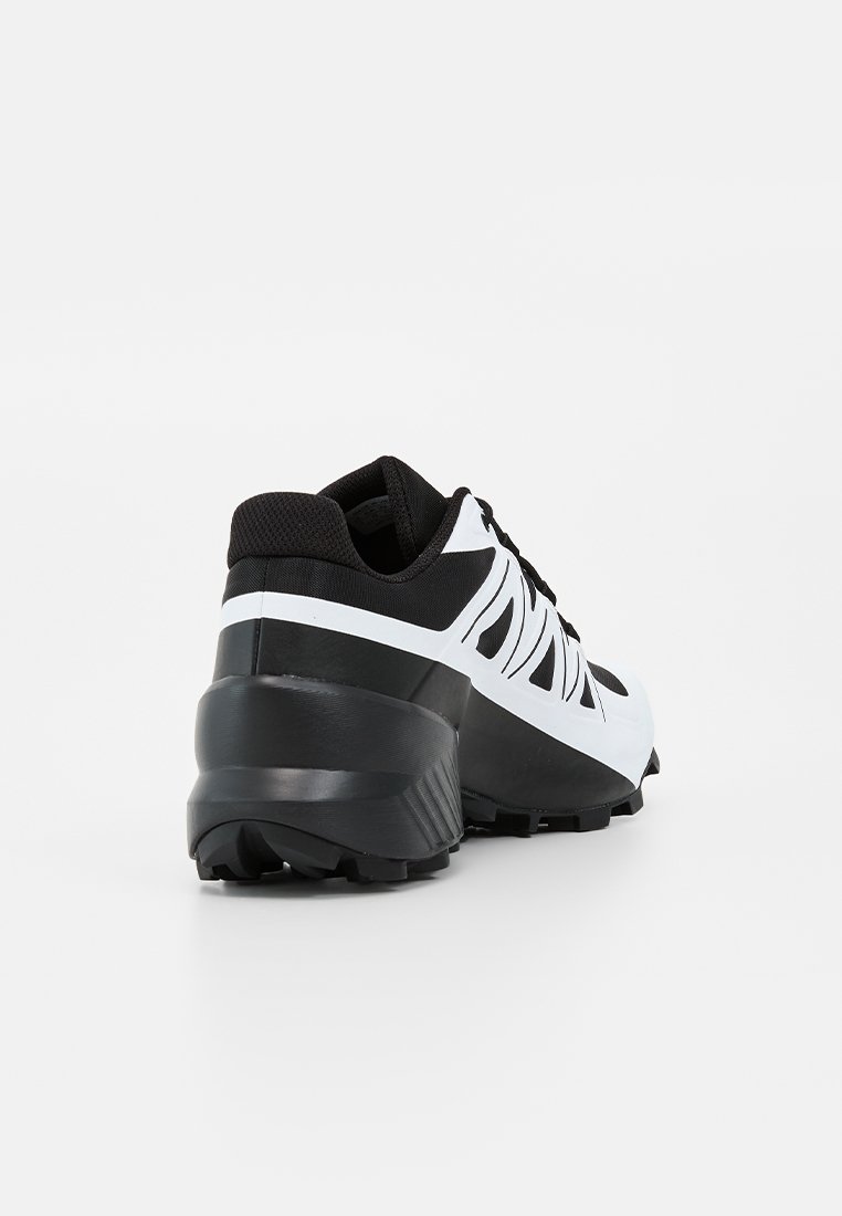 Chaussure de sport noire et blanche avec semelle épaisse et empeigne en mesh, vue de dos et légèrement de côté sur fond blanc.
