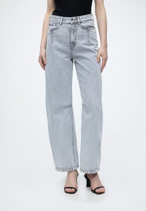 Person trägt hellgraue High-Waist-Straight-Jeans, kombiniert mit einem schwarzen ärmellosen Oberteil und schwarzen offenen Sandalen mit Absatz.