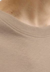 Beige T-shirt med rund hals fremstillet af glat, strækbart stof med en diskret ribbet halsudskæring. Fokuser på teksturen og det bløde udseende.