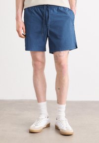 Shorts en coton bleu avec une taille élastique et un cordon de serrage. Comprend des poches latérales et une coupe droite, associés à des baskets blanches et des chaussettes.