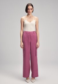 Licht beige geribde bodysuit met dunne bandjes, gecombineerd met hooggehad, wijde mauve cargo-broeken met zijzakken en een gladde textuur.
