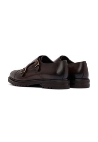 Een paar donkerbruine leren dubbelmonk strap dress schoenen met rubberen lugzolen, gekanteld om de buitenkant en de achterkant te tonen.