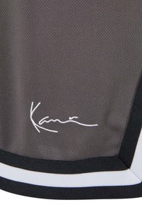 Tissu gris foncé avec signature cursive blanche "Kani" brodée près du bord inférieur, bordée de rayures noires et blanches.