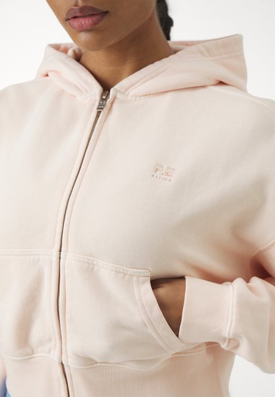 Haut de sweat à capuche zippé rose clair en mélange de coton doux, avec une poche kangourou, des poignets côtelés et un logo en relief sur la poitrine.