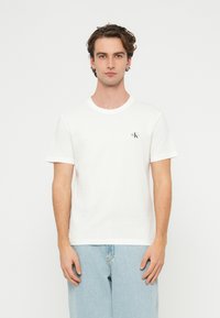 Fehér pamut póló kerek nyakkivágással és rövid ujjakkal, bal oldali mellrészen kis fekete logóval. Kényelmes szabás, puha anyagú.