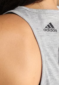 Canotta atletica grigia con design senza maniche, con un logo Adidas nero sul retro vicino al colletto. Texture liscia.