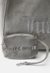 Szary zamszowy torebka z akcentami z cyrkonii, na której widnieje napis "Juicy Couture", z dodatkową mniejszą torebką przymocowaną srebrnym łańcuchem.