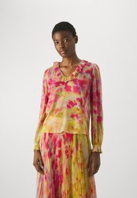 Blusa a maniche lunghe in tessuto leggero e trasparente con un motivo floreale colorato in rosa e giallo, con dettagli di colletto arruffato e polsini.