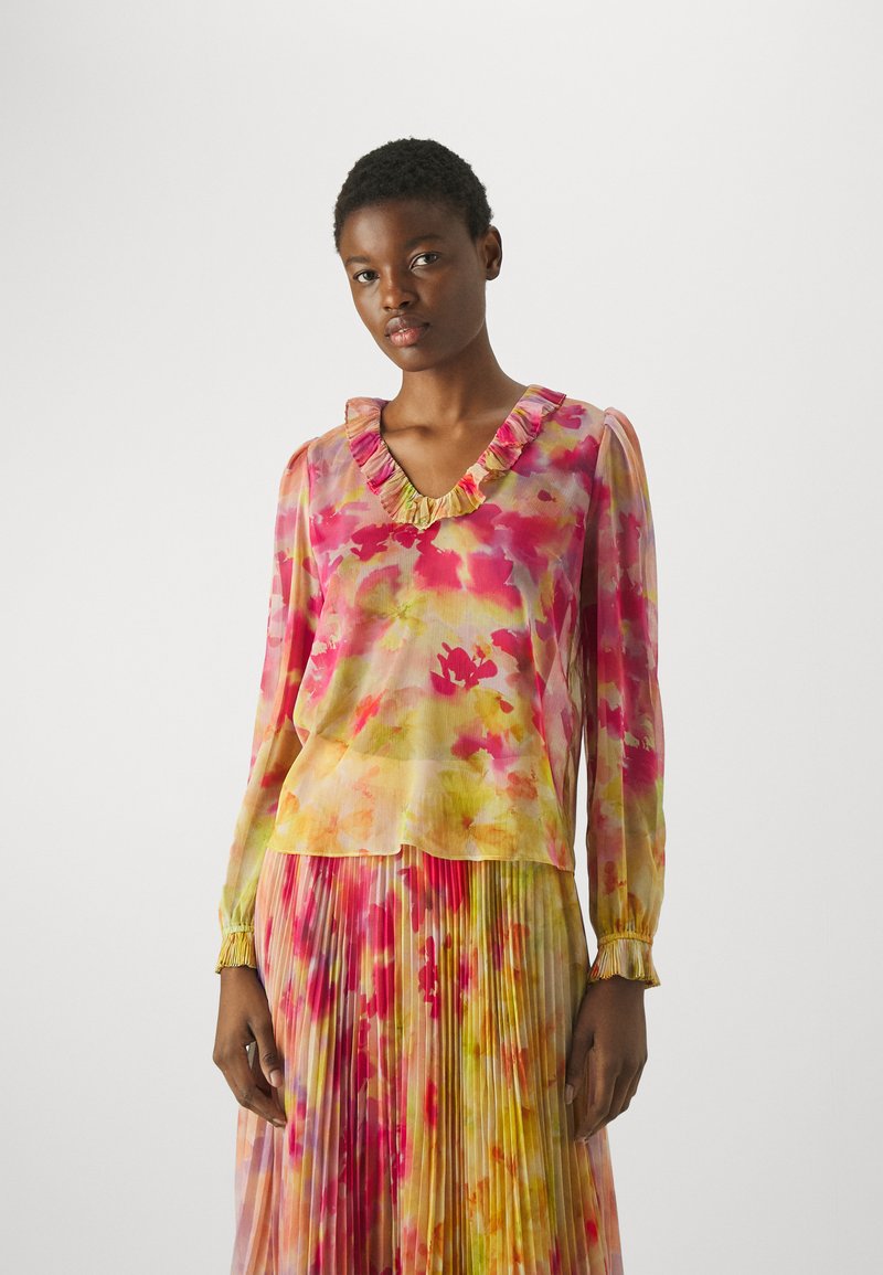 Blusa a maniche lunghe in tessuto leggero e trasparente con un motivo floreale colorato in rosa e giallo, con dettagli di colletto arruffato e polsini.