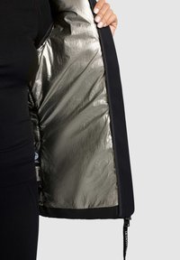 Black jacket with a shiny metallic silver interior lining, featuring a zippered closure and fabric tag visible on the inside.