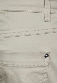 Beige katoenen broek met een gladde textuur, voorzien van zichtbare stikdetails en een metalen knoopaccent op de zak.