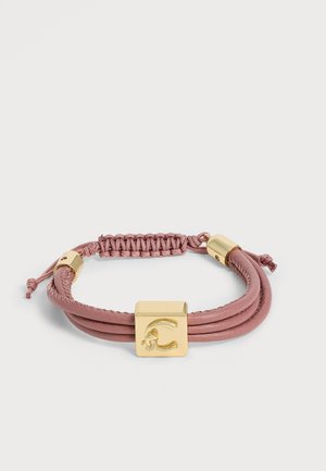 Pulsera de cordón rosa con detalles metálicos dorados y un charm central cuadrado dorado con la letra C grabada.