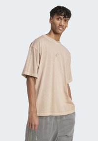 Beige oversized t-shirt with short sleeves, featuring a subtle three-stripe design on the sleeves and a small logo on the chest.