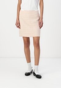 Saia mini de tweed rosa com um acabamento texturizado, apresentando uma bainha desfiada. Usada com uma blusa branca e sapatos pretos, acompanhada de meias brancas.