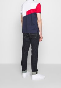 Polo tričko s barevným blokem v námořnické modři, bílé a červené; spárované s tmavými denimovými džínami. Bílé tenisky s detailem ohrnutého lemu.