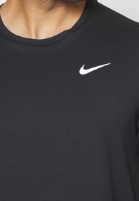 Czarna koszulka sportowa z przewiewnego materiału, z okrągłym dekoltem i małym białym logo Nike na piersi.