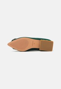 Scarpa con tacco alto in velluto verde, punta affusolata, tacco in gomma cremosa e piatta, e un accento di gioielli neri sulla punta, con suola texturizzata.