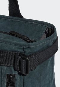 Dark green, textured fabric bag with a top zipper, black strap, and buckle closure. Features a cylindrical shape for storage.