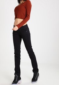 Crop top rouge à manches longues côtelé associé à un jean skinny noir et des bottines noires avec des détails en œillets et des semelles transparentes.