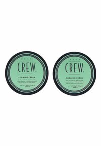 Två runda burkar med American Crew stylingkräm. Gröna etiketter med svart text som anger medelhårt grepp och glans, 50g vardera, slät finish.