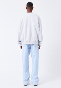 Sudadera gris de corte relajado, con puños y dobladillo acanalados, combinada con jeans rectos de color azul claro. Diseño simple y sin adornos con una textura suave.
