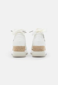 Zapatillas blancas con una parte superior texturizada, una entresuela de yute trenzado y lazos de satén en la parte posterior. Material suave y diseño minimalista.