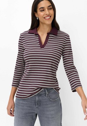 Donna che indossa una maglia a righe viola e bianca a maniche lunghe con colletto, sorridente, abbinata a jeans di denim grigi.
